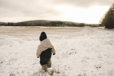 Volle Länge Rückansicht von Mädchen zu Fuß auf schneebedeckten Land bei Sonnenuntergang - MASF24718