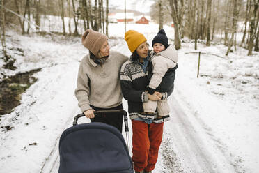 Mature woman carrying daughter while walking with girlfriend on snow - MASF24720