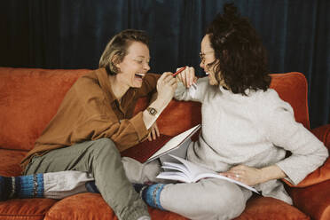 Fröhliches lesbisches Paar sitzt zusammen auf dem Sofa zu Hause - MASF24740