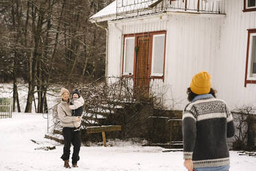 Ältere Frau geht auf lächelnde Freundin zu, die ihre Tochter im Schnee trägt - MASF24745