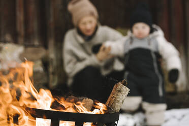 Burning wood in fire pit against woman and daughter during winter - MASF24752