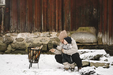 Mutter zeigt auf brennende Feuerstelle zu Tochter, während sie auf Schnee kauert - MASF24756