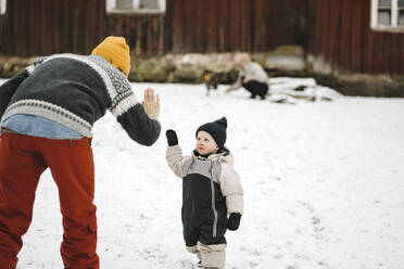 Rear view of mother giving high-five to daughter during winter - MASF24757