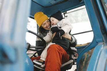 Fröhliche Mutter mit Tochter im Traktor sitzend im Winter - MASF24759