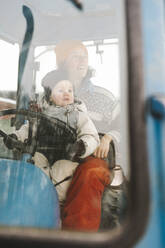 Mutter und Tochter im Traktor sitzend durch die Windschutzscheibe gesehen - MASF24760