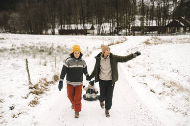 Lesbisches Paar in voller Länge, das seine Tochter in den Schnee zieht - MASF24779
