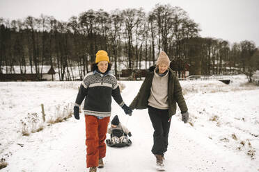 Smiling lesbian couple pulling daughter on toboggan during winter - MASF24783