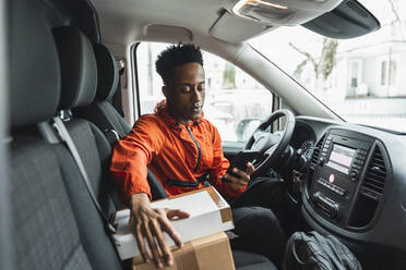 Junger männlicher Fahrer benutzt sein Smartphone, während er im Lieferwagen sitzt - MASF24823