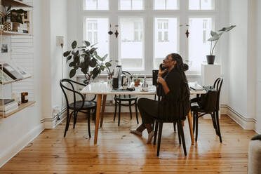 Young female professional talking on mobile phone sitting in home office - MASF24864