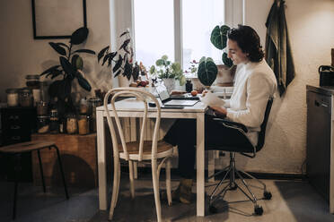 Geschäftsmann mit Laptop sitzend und schreibend bei der Arbeit von zu Hause aus - MASF24875