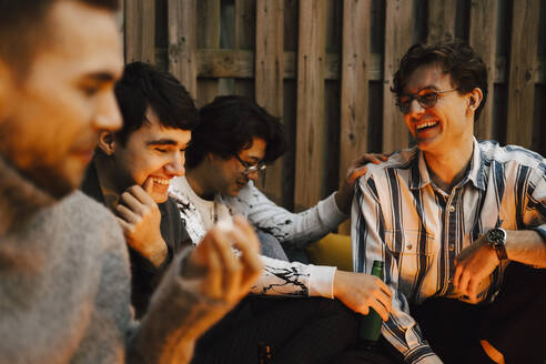 Happy young male friends talking while spending leisure time in balcony - MASF24907