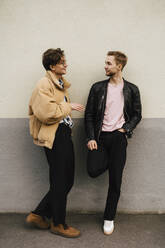 Männliche Freunde reden miteinander, während sie sich an eine beigefarbene Wand lehnen - MASF24921