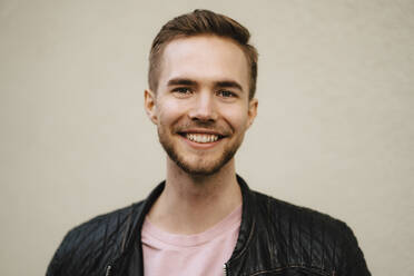 Lächelnder junger Mann mit Bartstoppeln an der Wand - MASF24930