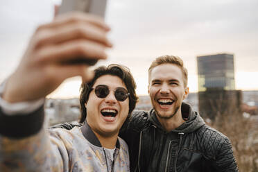 Cheerful male friends taking selfie on smart phone - MASF24937