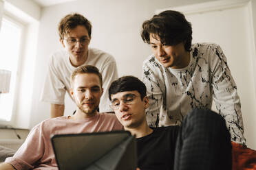 Männliche Freunde teilen sich ein digitales Tablet im Wohnzimmer - MASF24964