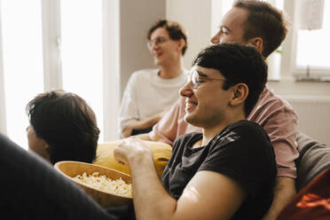 Multiethnische männliche Freunde essen Popcorn beim Sportschauen im Wohnzimmer - MASF24965