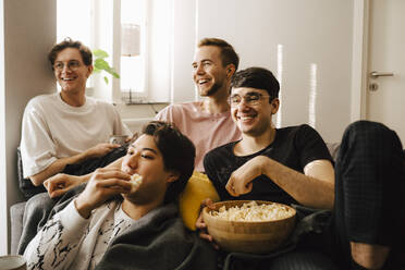 Lächelnde männliche Freunde essen Popcorn, während sie zu Hause Sport schauen - MASF24966