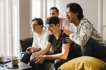 Lächelnde multiethnische männliche Freunde spielen ein Videospiel im Wohnzimmer - MASF24967