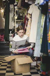 Junge Unternehmerin betrachtet verpackte Kleidung in einer Boutique - MASF24973