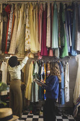 Rückansicht des Besitzers, der die Kleidung ordnet, während die Unternehmerin in der Boutique Notizen macht - MASF24987