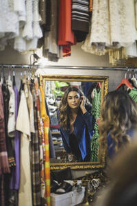 Weiblicher Besitzer schaut in den Spiegel, während er in einem Bekleidungsgeschäft steht - MASF25004