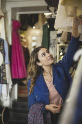 Smiling female owner arranging clothes on rack in store - MASF25010