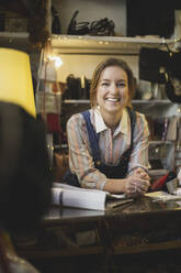 Porträt einer lächelnden Besitzerin, die sich in einem Geschäft auf einen Tisch stützt - MASF25017