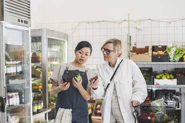 Eine Frau zeigt einem Kunden beim Einkaufen im Geschäft ein Produkt - MASF25037