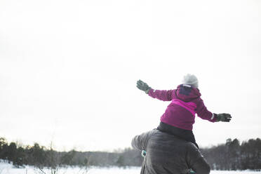 Rear view of father carrying daughter on shoulders during winter - MASF25105