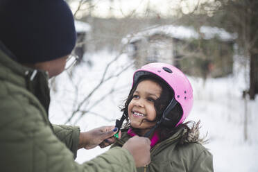 Smiling girl looking at mother help in wearing helmet during vacation - MASF25112