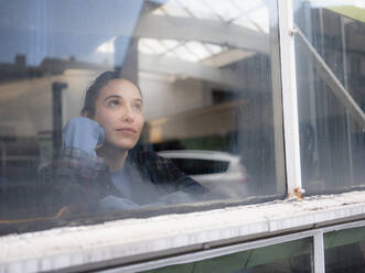 Female mechanic contemplating seen through window at workshop - KNSF08862