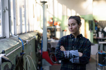 Mechanikerin mit verschränkten Armen in der Werkstatt stehend - KNSF08863