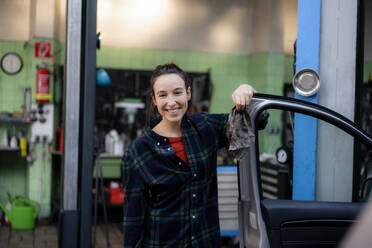 Lächelnde Mechanikerin beim Öffnen der Autotür in der Werkstatt - KNSF08882