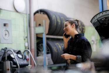 Weiblicher Mechaniker schaut weg, während er in der Werkstatt mit seinem Smartphone telefoniert - KNSF08884