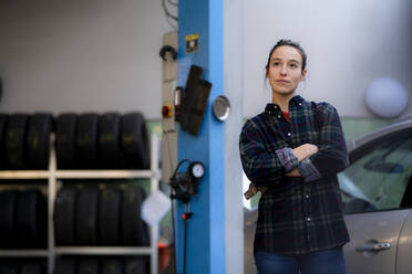 Weiblicher Mechaniker mit verschränkten Armen, der in der Werkstatt steht und nachdenkt - KNSF08886