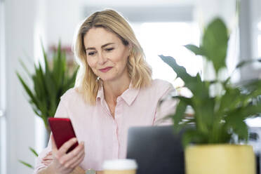 Smiling businesswoman using smart phone at home office - WPEF04940