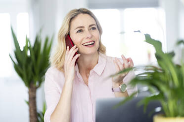 Geschäftsfrau schaut weg, während sie im Büro zu Hause mit ihrem Smartphone telefoniert - WPEF04941