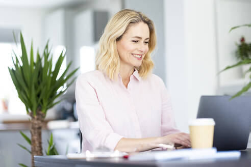 Lächelnde Geschäftsfrau, die im Büro zu Hause am Laptop arbeitet - WPEF04947