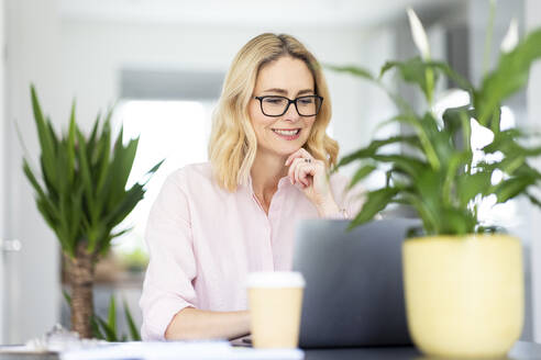 Smiling female professional with eyeglasses working at home office - WPEF04951