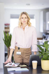 Businesswoman standing near desk at home office - WPEF04958