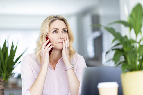 Contemplating businesswoman talking on smart phone at home office - WPEF04965