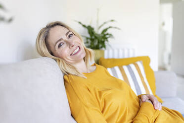 Lächelnde reife Frau sitzt auf dem Sofa zu Hause - WPEF04978