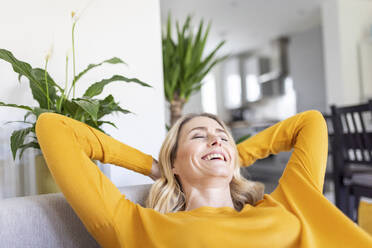 Smiling woman with hands behind head sitting at home - WPEF04979