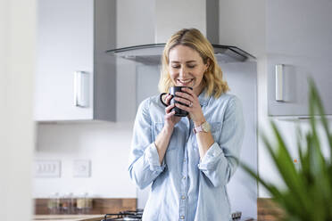 Lächelnde Frau riecht Tee in der Küche zu Hause - WPEF05004