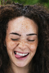 Cheerful young curly haired woman with eyes closed sticking out tongue - JCMF02031