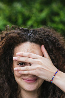 Lächelnde Frau mit lockigem Haar, die durch die Finger schaut - JCMF02033
