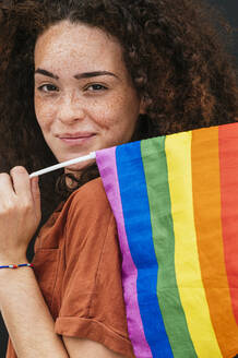 Beautiful smiling curly haired woman with rainbow flag - JCMF02045