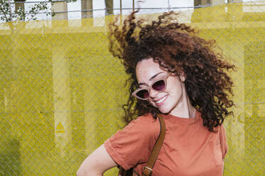 Smiling young woman tossing hair in front of yellow fence - JCMF02066