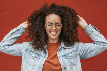 Playful woman sticking out tongue with hands in curly hair - JCMF02073