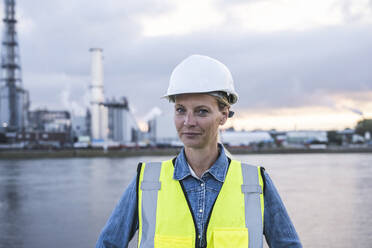 Mature female professional wearing hardhat near river - UUF23766